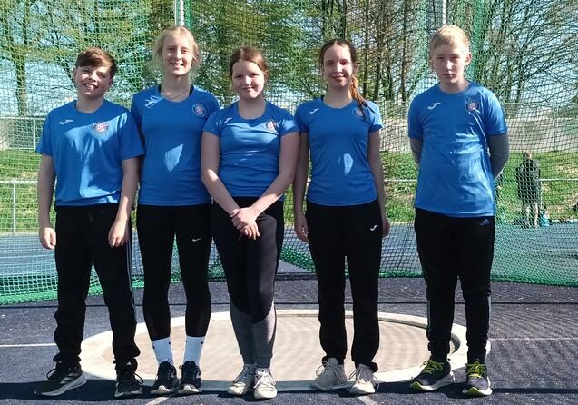 F&uuml;nf Sportler*innen stehen in einem Wurfk&auml;fig