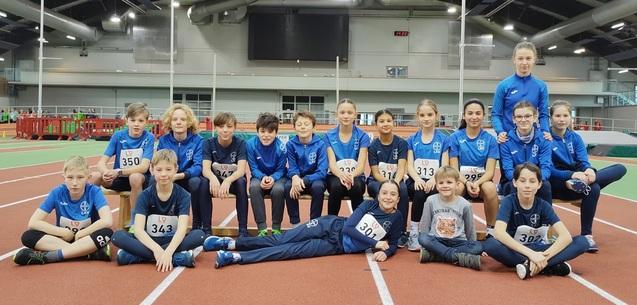 Große Kindergruppe sitzt und kniet in einer Sporthalle