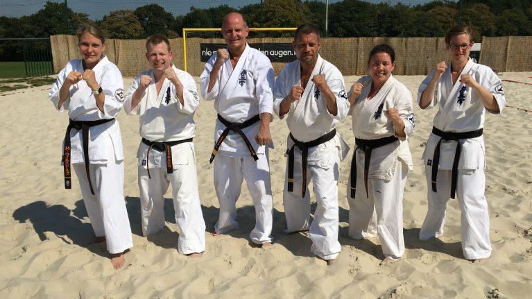 Sechs Personen mit wei&szlig;en Karate Anz&uuml;gen stehen im Sand