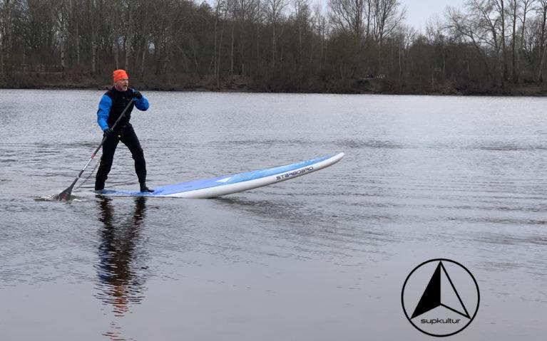 Ein Stand Up Paddler steht auf seinem Board und die Spitze ragt in die Luft