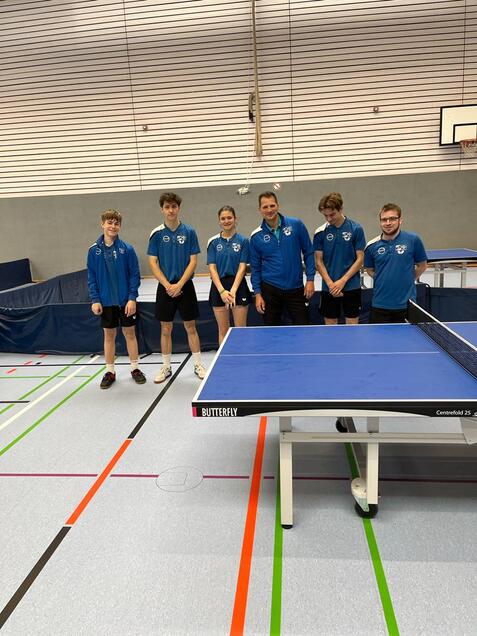 Sechs Personen stehen hinter einer blauen Tischtennisplatte