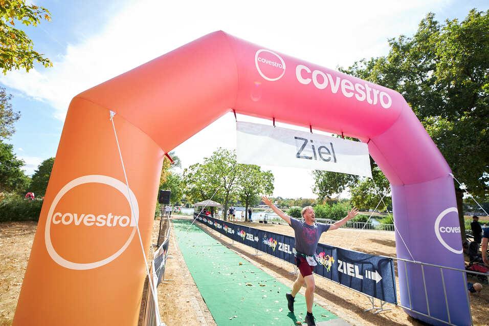 Ein Mann läuft mit hochgerissenen Armen durch den bunten Covestro-Zielbogen