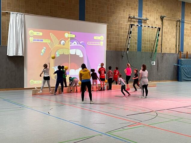 Zwei Gruppen Kinder spielen gegeneinander ein Spiel auf einer gro&szlig;en Leinwand