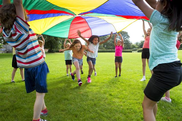 Zwei Kinder laufen unter einem Schwungtuch, das  von anderen Kindern hochgehalten wird