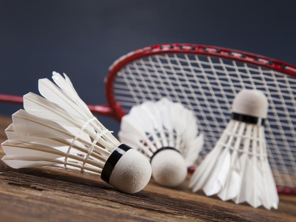 Drei Federbälle liegen auf einem Holztisch, mit einem Badmintonschläger im Hintergrund.