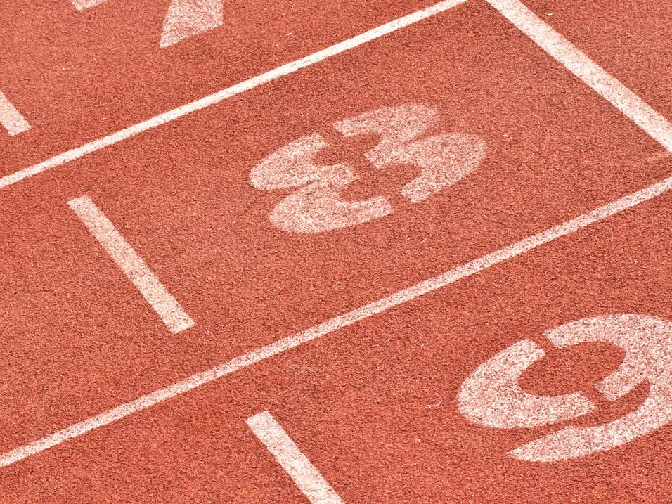 Nahaufnahme von Laufbahnmarkierungen mit den Nummern 7, 8 und 9 auf einem roten Sportplatz.