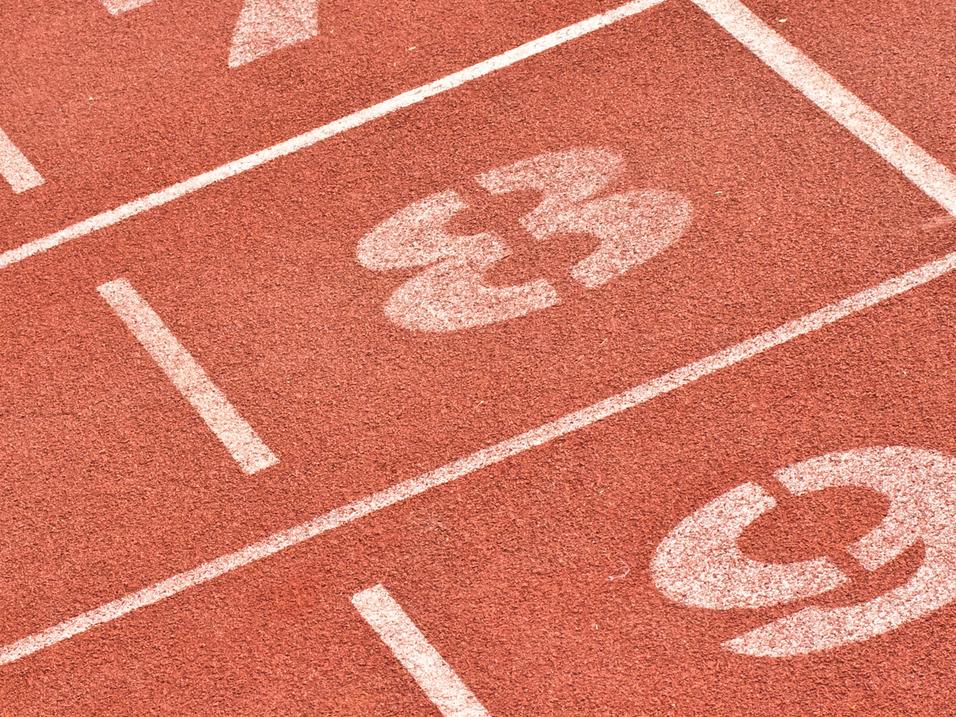 Nahaufnahme von Laufbahnmarkierungen mit den Nummern 7, 8 und 9 auf einem roten Sportplatz.