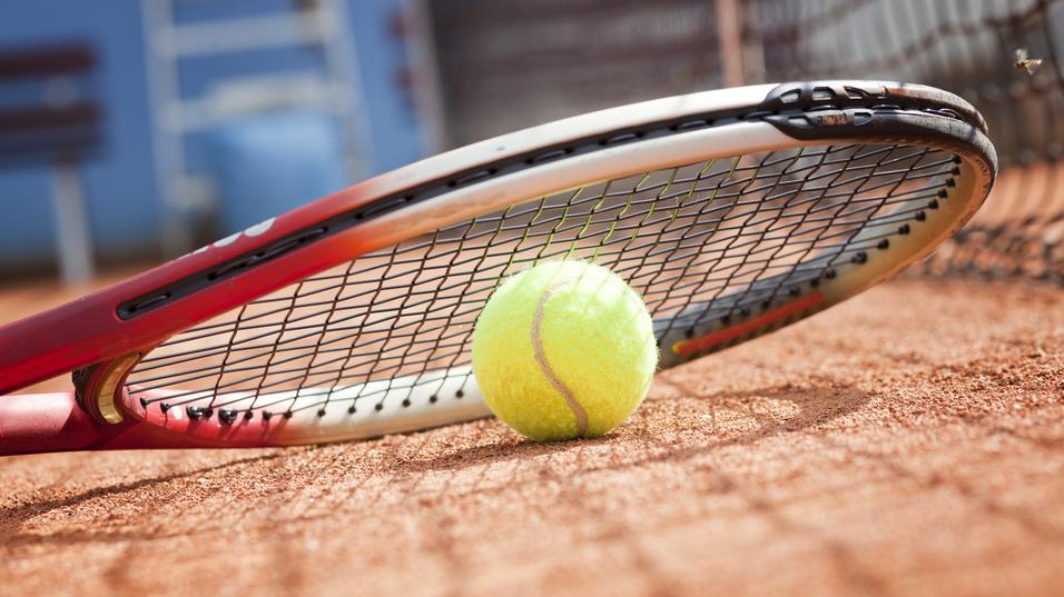 Tennisball liegt auf einem Platz neben einem Tennisracket auf dem Sandboden.