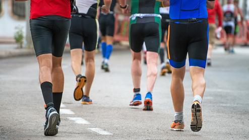 Gruppe von Männern in Sportkleidung joggt auf einer asphaltieren Straße, während sie dem Rennen folgen.